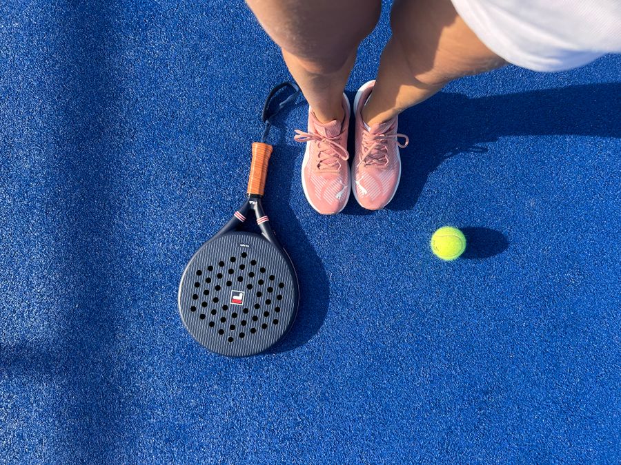Padel shoes, racket and ball on a blue court